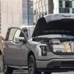 A woman loading luggage into the frunk of a silver 2024 Ford F-150 Lightning.