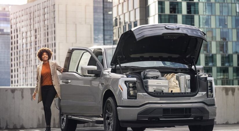 A woman loading luggage into the frunk of a silver 2024 Ford F-150 Lightning.