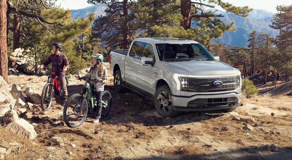 A pair of bicyclists and a silver 2024 Ford F-150 Lighting off-roading on a mountain.