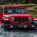 A red 2024 Jeep Wrangler Rubicon is shown fording a river after visiting a Jeep Wrangler dealer.