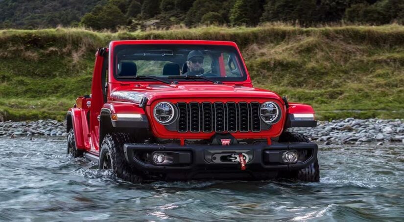 A red 2024 Jeep Wrangler Rubicon is shown fording a river after visiting a Jeep Wrangler dealer.