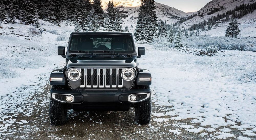 A black 2024 Jeep Wrangler is shown driving through snow.