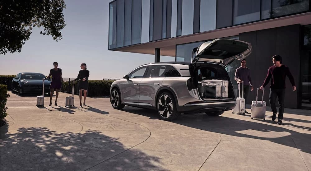 A silver 2025 Lucid Air Gravity is shown parked on a driveway near people with luggage.