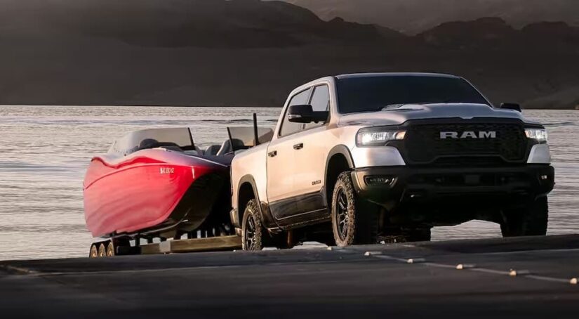 A silver 2025 Ram 1500 is shown towing a boat.