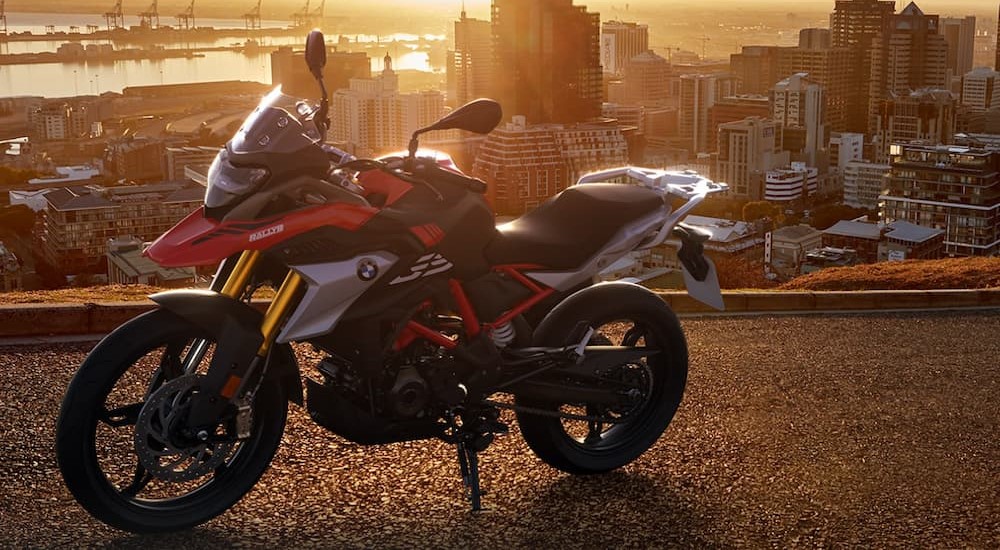 A multi-colored 2023 BMW G 310 GS is shown parked near a city.