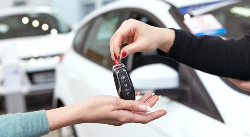 A car dealership employee is shown handing a key fob to a customer.