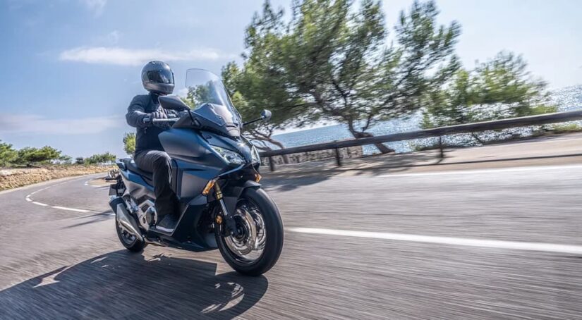 A person in motorcycle gear riding a grey Honda Forza 750 on the highway.