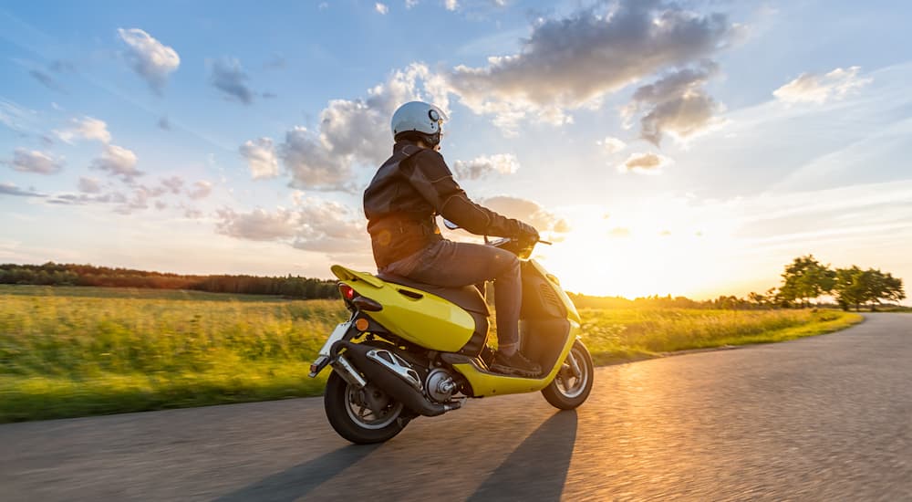 A man riding a yellow moped scooter along grassy fields.