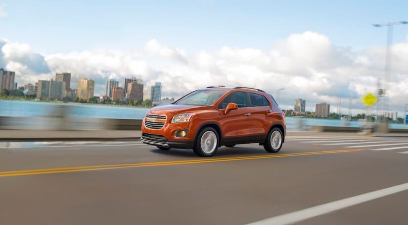 An orange 2015 Used Chevy Trax for sale driving past a city harbor.