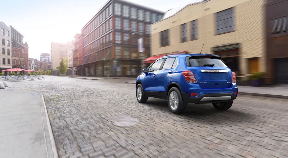 A blue 2017 Chevy Trax driving away from the camera on a cobblestone street.
