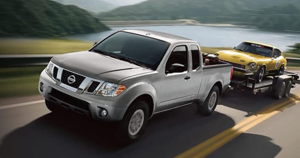 A silver 2020 Nissan Frontier is shown towing a trailer near a lake.