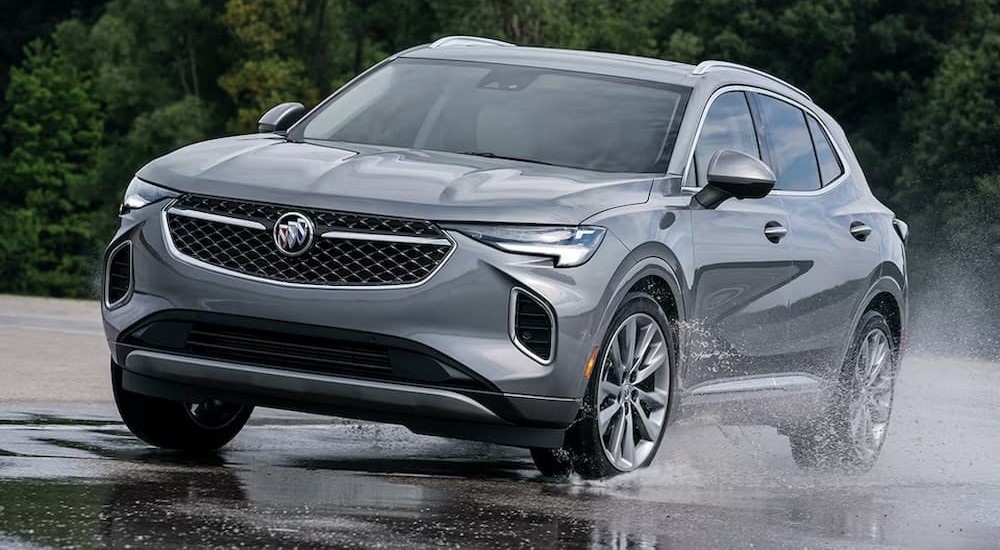 A gray 2023 Buick Envision is shown driving on a puddle.