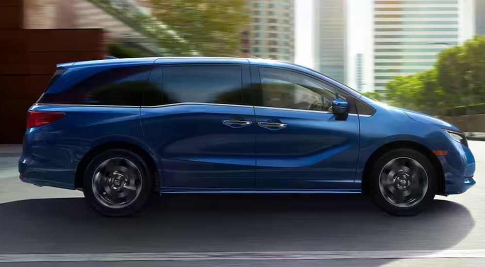 A blue 2024 Honda Odyssey Elite is shown driving near city buildings.