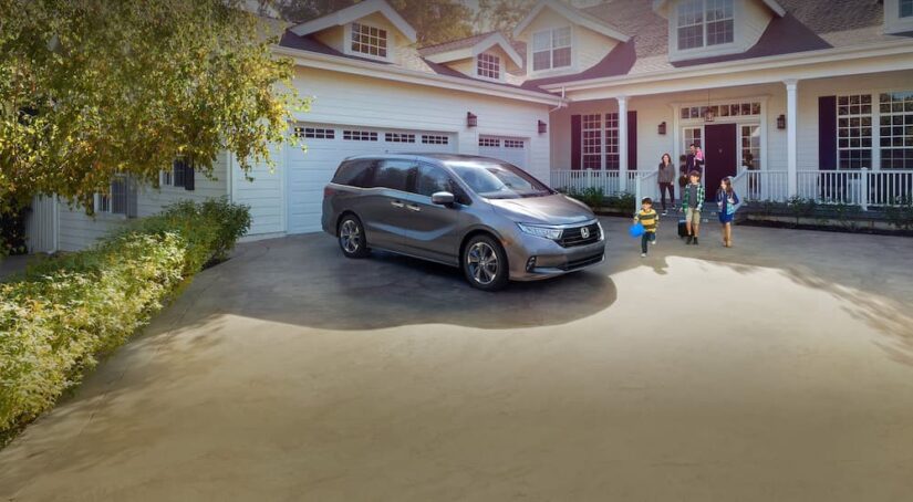 A gray 2024 Honda Odyssey is shown parked on a driveway near a family.