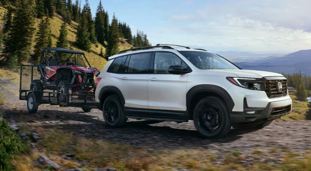 A white 2024 Honda Passport Black Edition is shown towing a trailer off-road.