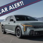 A grey 2025 Kia K4 is shown driving on an open road with a New Car Alert banner overlayed.