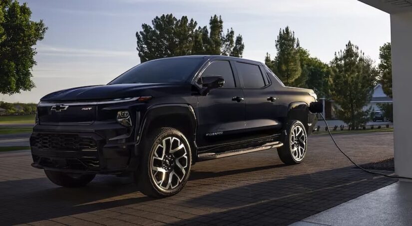 An upcoming black Silverado PHEV RST is shown charging near a Chevy dealer.