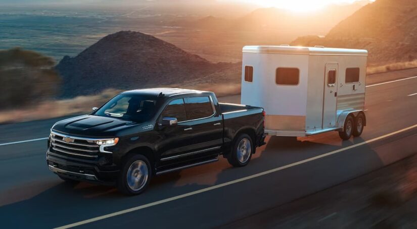 A black 2024 Chevy Silverado 1500 High Country towing a trailer on a coastal road.