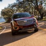 A red 2019 Cadillac XT5 is shown driving from a used car dealership.