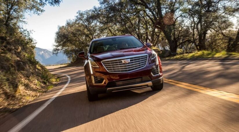 A red 2019 Cadillac XT5 is shown driving from a used car dealership.