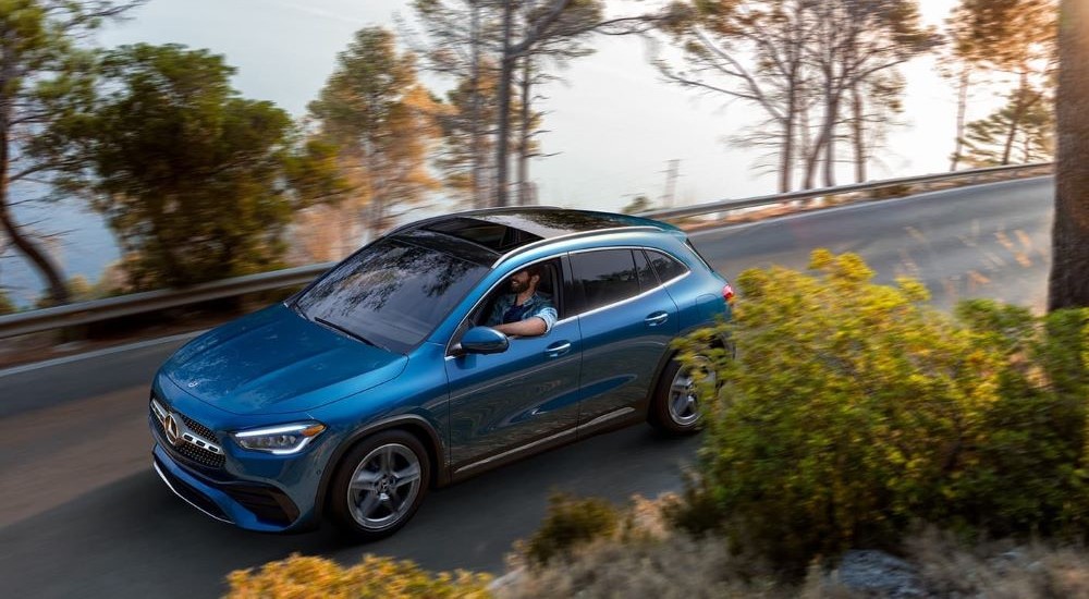 A blue 2022 Mercedes-Benz GLA 250 is shown driving by a lake.