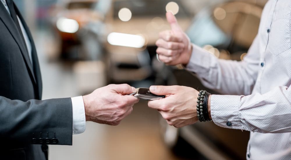 A person is shown receiving a key fob for one of many used SUVs for sale. 