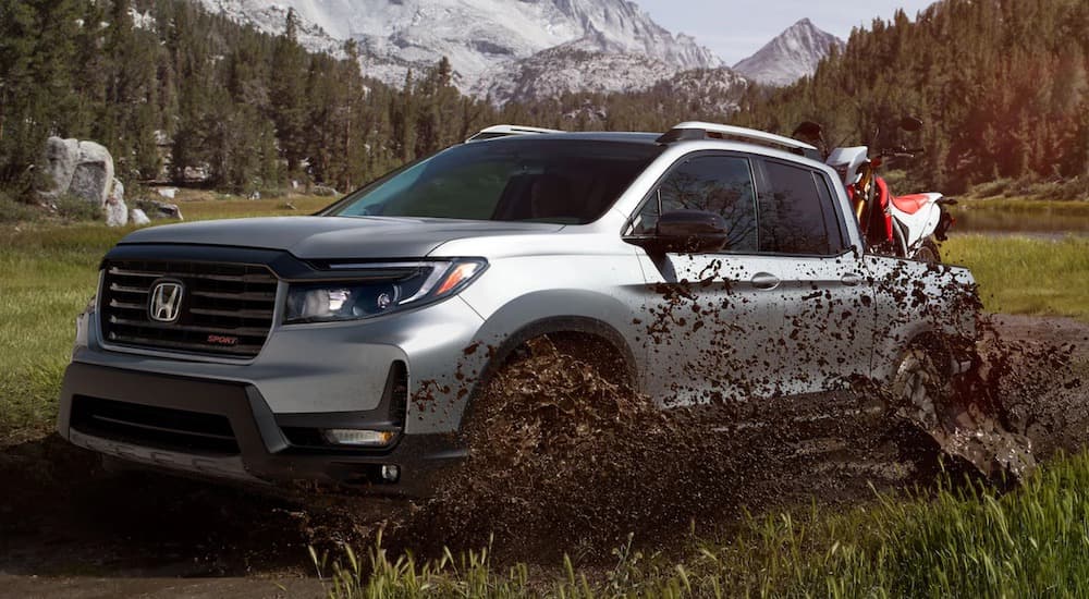 A silver 2024 Honda Ridgeline is shown driving over a muddy trail.