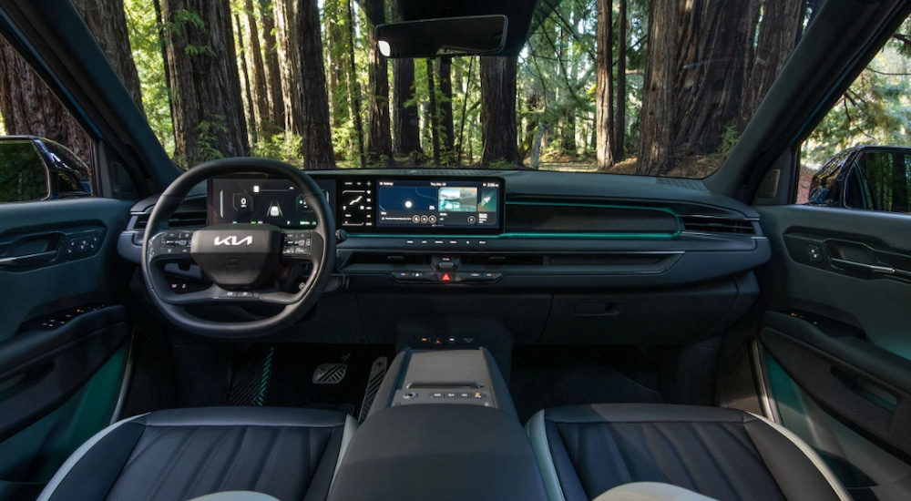 The front seats and dashboard in a 2024 Kia EV9 parked in the woods.