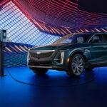 A teal 2024 Cadillac LYRIQ plugged in to charge under colorful modern lights.
