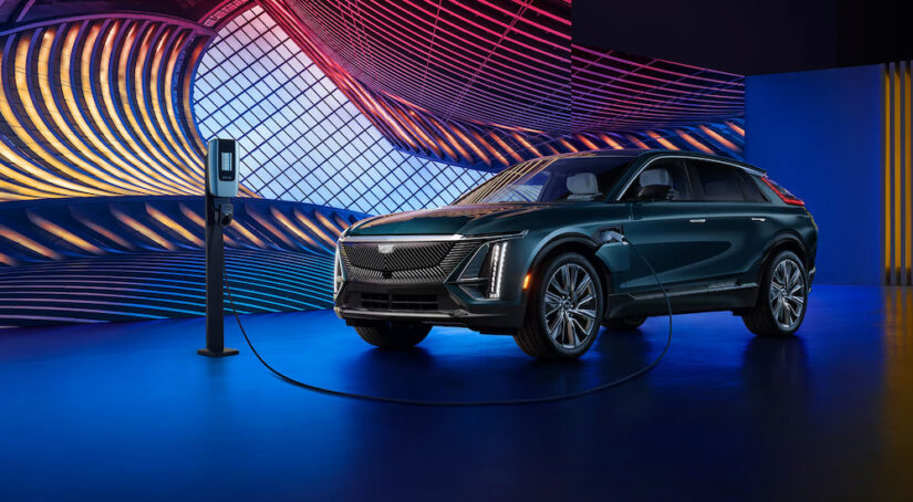A teal 2024 Cadillac LYRIQ plugged in to charge under colorful modern lights.