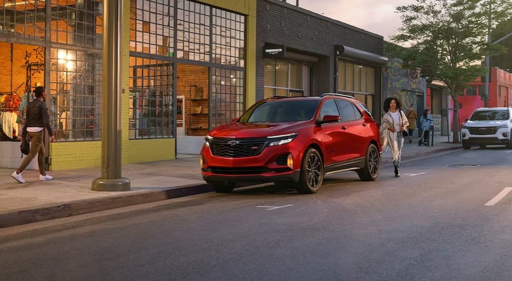 A red 2024 Chevy Equinox RS parked in front of a downtown store.