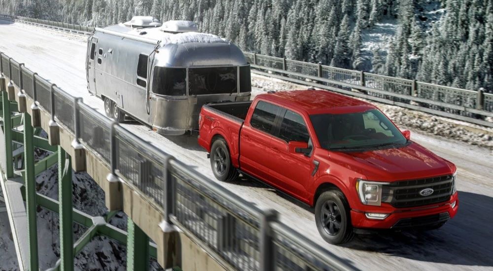 A red 2025 Ford F-150 Sport towing a trailer across a snowy bridge.