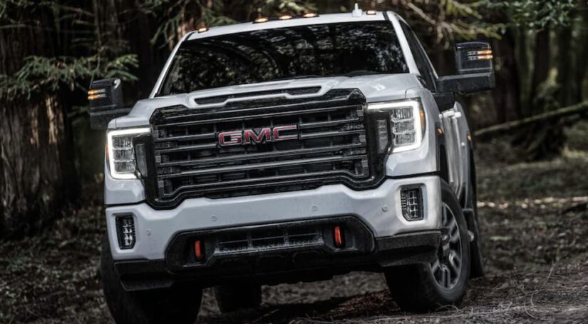 A front angle view of a white 2024 GMC Sierra 2500 HD AT4 driving in a forest.