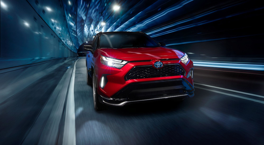 A red 2024 Toyota RAV4 Prime XSE driving through a tunnel with blue lighting.