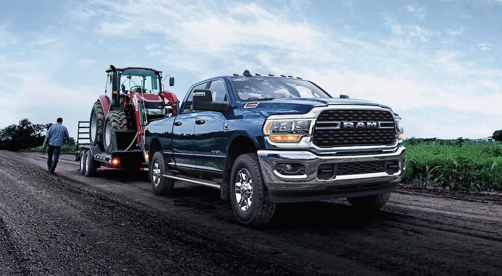 A blue 2024 Ram 2500 Cummins is shown from the front at an angle while towing a tractor.