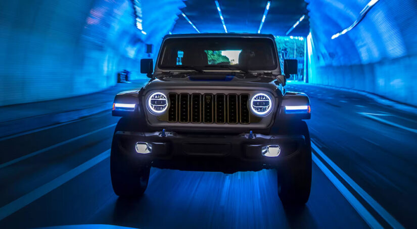A silver 2024 Jeep Wrangler 4xe driving toward the camera through a blue tunnel.