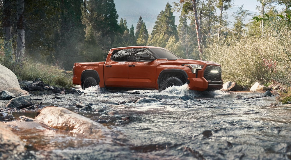 An orange 2024 Toyota Tundra TRD is shown crossing a river.