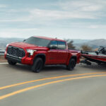 A red 2024 Toyota Tundra is shown from the front while towing a boat.