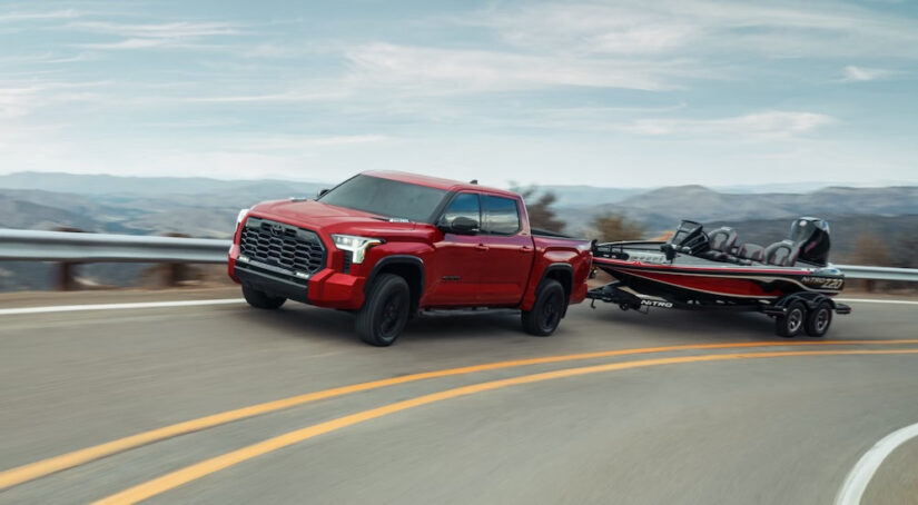 A red 2024 Toyota Tundra is shown from the front while towing a boat.