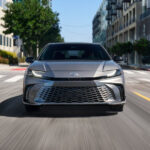 Head on view of a silver 2025 Toyota Camry XSE driving on a city street.