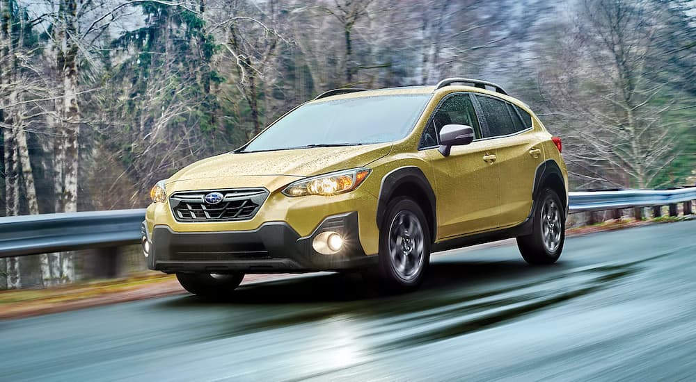 A yellow 2023 Subaru Crosstrek Sport is shown driving on a wet highway.