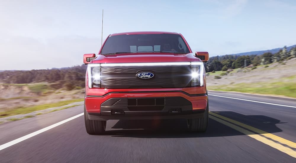 A red 2024 Ford F-150 Lightning driving on an open road to a Ford dealer.