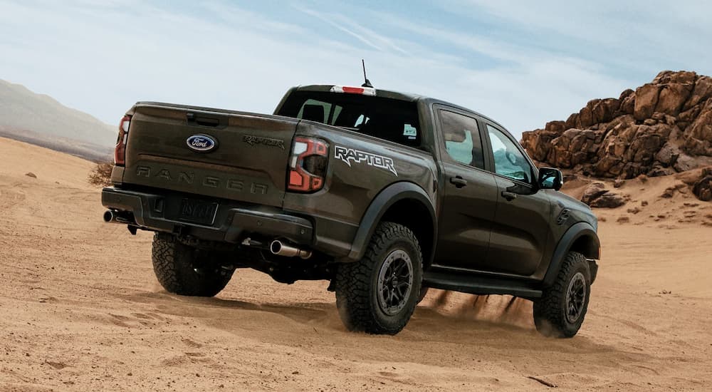 A dark 2024 Ford Ranger Raptor is driving on sand.