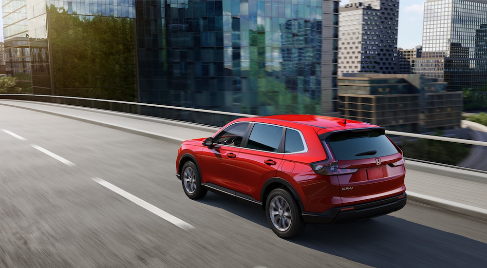 Rear overhead view of a red 2024 Honda CR-V EX driving through the city.