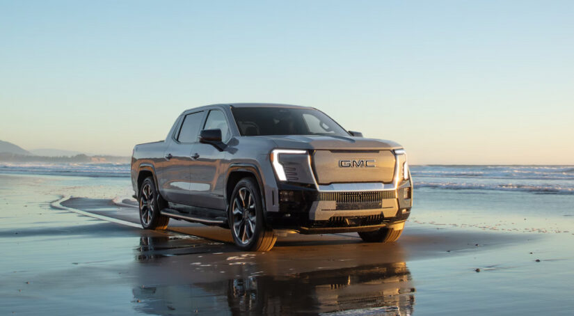 A silver 2024 GMC Sierra EV Denali Edition 1 driving on a shoreline after viewing trucks for sale.