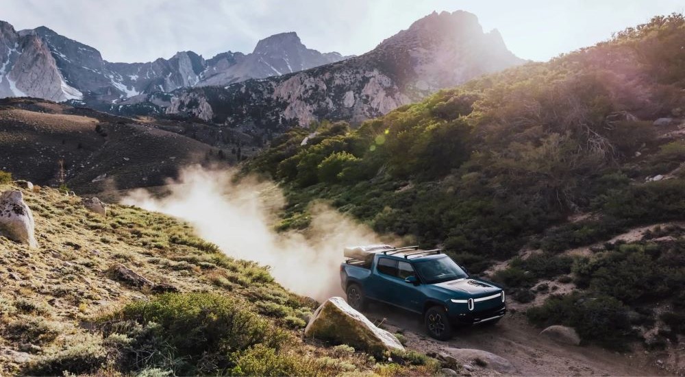 A blue 2024 Rivian R1T is shown driving off-road.