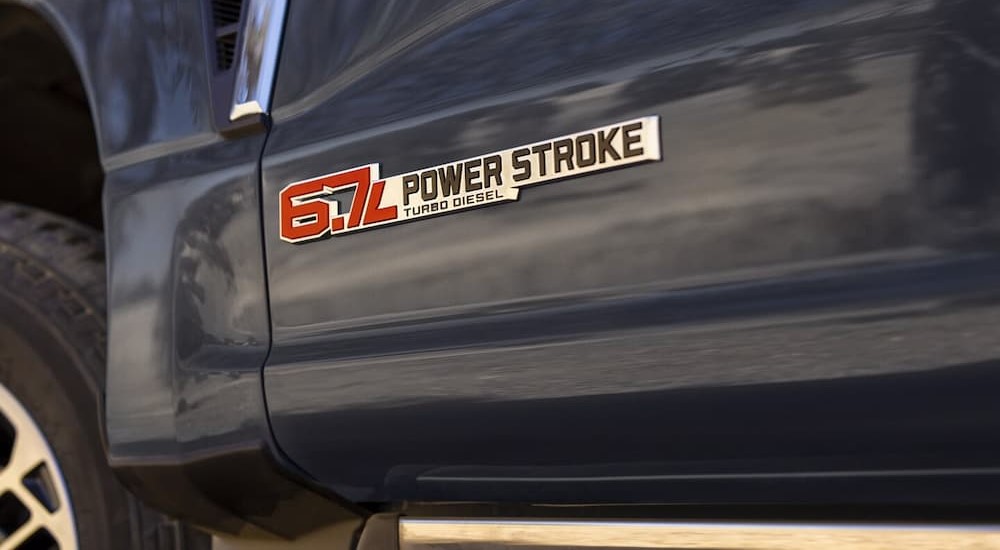 A close-up of a 6.7L Power Stroke badge is shown on a gray 2024 Ford F-350.