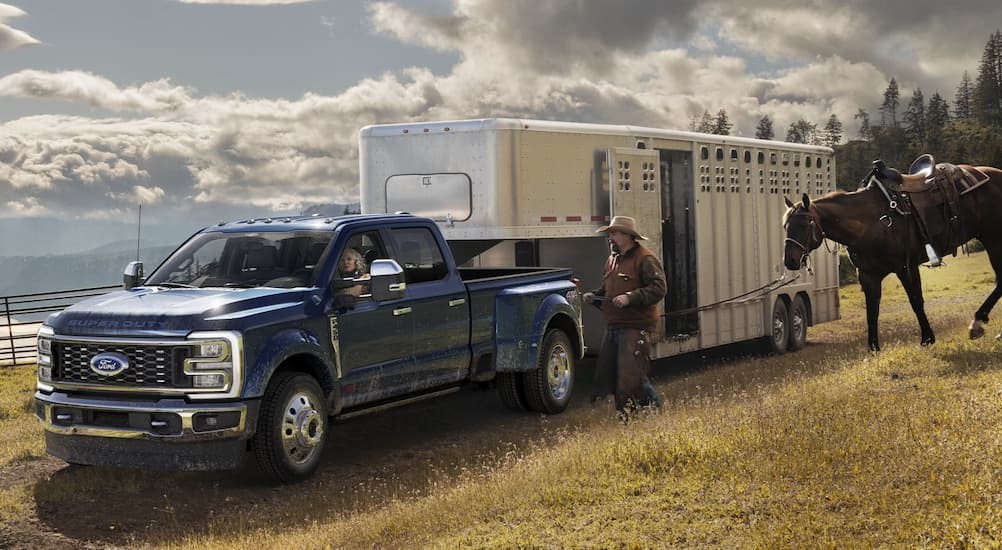 A blue 2024 Ford F-450 is shown towing a horse trailer.