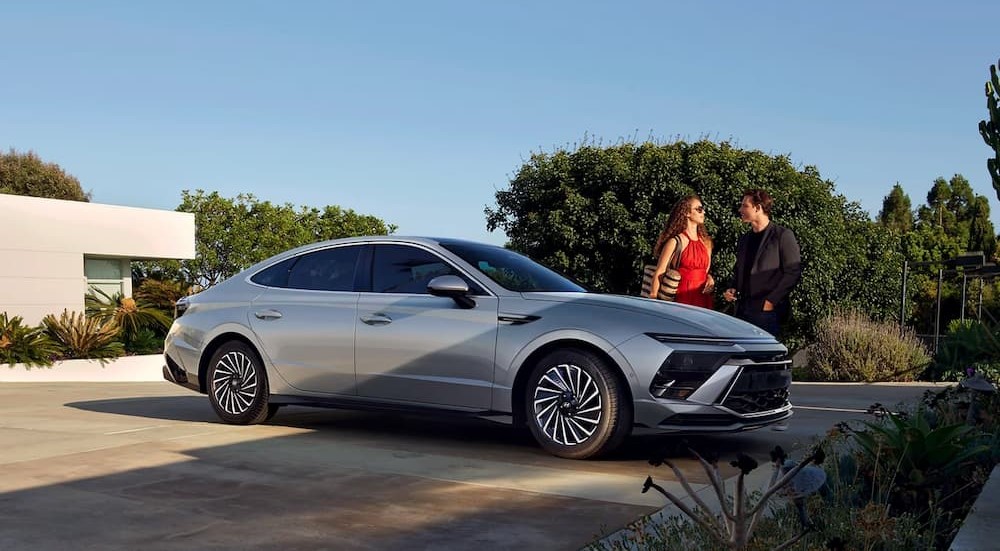 A silver 2024 Hyundai Sonata Limited Hybrid is shown parked near two people talking.