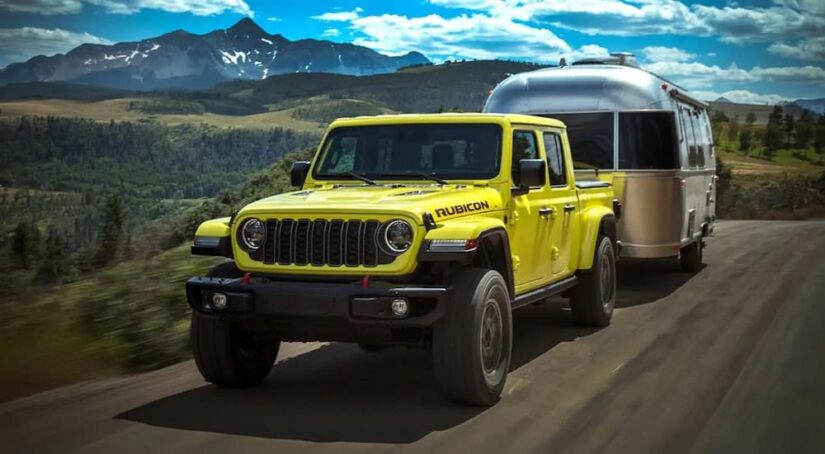 A popular Jeep Gladiator for sale, a yellow 2024 Jeep Gladiator Rubicon, is shown towing a trailer near a mountain.